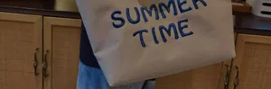 Close-up shot of the beige canvas tote bag showing blue embroidered Summer Time text.