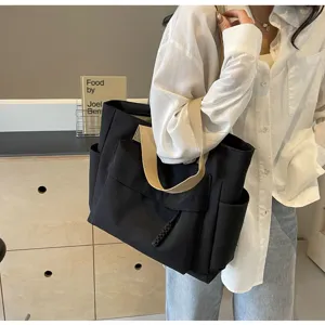Detail view of black canvas tote bag with beige straps and side pockets, large capacity style.