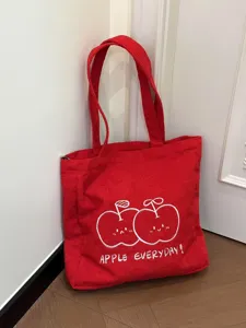 Red corduroy tote bag detail showing cute embroidered apple design and everyday text.