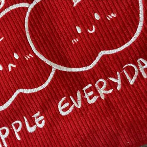 Red corduroy tote bag detail with cute apple embroidery and everyday letter pattern.