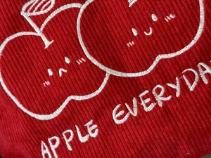 Detailed close-up of red corduroy tote bag featuring cute white apple embroidery design.