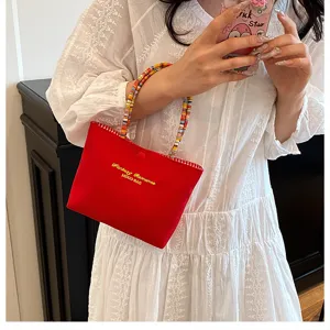 Vue détaillée d'un sac à main rouge avec anses perlées colorées et texte brodé stylé.