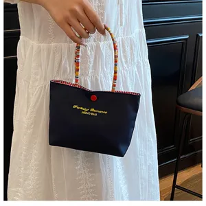 Vue détaillée du mini sac à main mignon avec des lettres brodées et des poignées perlées.
