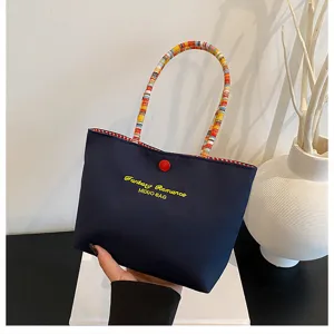 Gros plan du sac à main brodé bleu foncé avec poignées tissées colorées et bouton rouge.