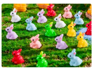Primo piano di statuette di coniglietti in resina colorata su muschio per micro-paesaggio.