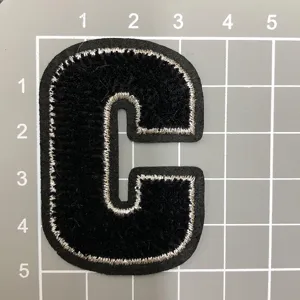 Schwarzer Buchstabe C bestickter Aufnäher Detail, Filzstoff mit silbernem Rand, Zubehör.