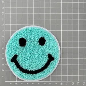 Close-up of mint green round smiley face towel embroidery patch with black facial details.