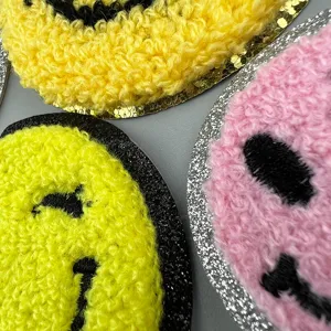 Gros plan sur les écussons brodés éponge smiley duveteux avec bordure pailletée pour vêtements.