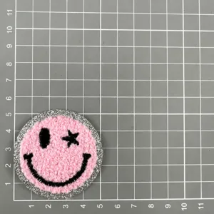Écusson brodé éponge rose visage smiley avec bordure scintillante argentée pour vêtements.