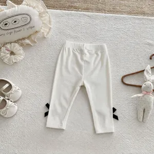 Infant baby white ribbed leggings featuring cute black bow details at cuffs, soft toddler pants.