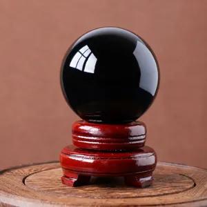 Detailed close-up of a polished black obsidian crystal sphere on a classic wooden base.