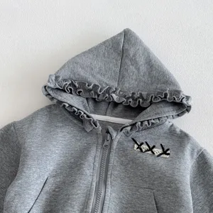 Detailed close-up of infant grey hooded jacket with cute ruffles and front bow decoration.