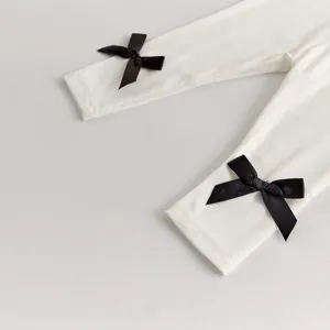 Detail shot of toddler girl white ribbed leggings featuring elegant black ribbon bow accents.