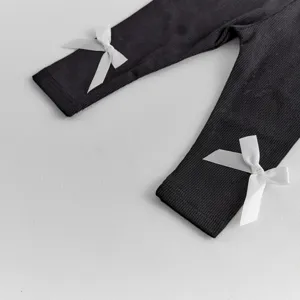 Close-up detail of infant baby black ribbed leggings featuring cute white bow accents at the cuffs.