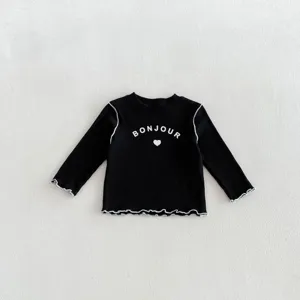 Dettaglio t-shirt nera a costine maniche lunghe bimbo con bordo volant e stampa.