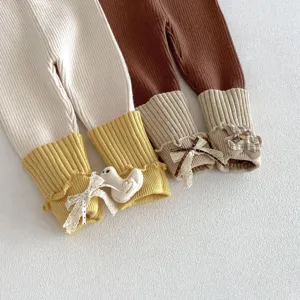Detailed view of baby knitted leggings featuring ribbed cuffs, bows and cute plush decorations.