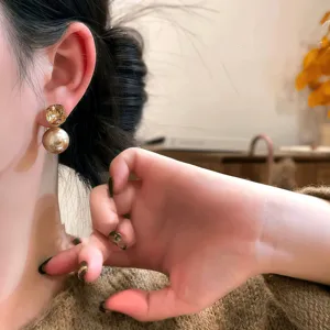 Close-up detail of luxury champagne gold diamond and pearl double-layer stud earrings.