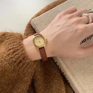 Close-up of a women's gold polygon quartz watch with a brown leather strap worn on wrist.