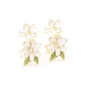 Dettaglio di orecchini a fiore smaltato bianco dorato, doppio strato e foglie verdi eleganti.