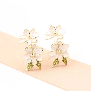 Eleganti orecchini a lobo con fiori smaltati bianchi placcati in oro e foglie verdi, gioielli.
