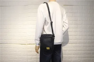 Detail view of black vertical leather shoulder bag worn by model, casual outdoor style.