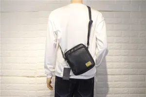 Detail view of black leather vertical messenger bag worn on back, showing adjustable strap.