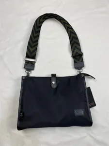 Detailed view of black nylon crossbody shoulder bag featuring a patterned wide strap and zipper.