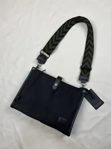 Close-up of black nylon messenger bag with green chevron wide strap and brand logo tag.