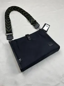 Detailed view of the black nylon messenger bag with wide chevron strap and metal hardware.