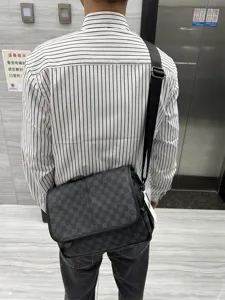 Vue détaillée du sac messager à carreaux gris et noirs pour homme, porté en bandoulière avec sangle.