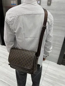Vue détaillée du sac messager à carreaux marron porté au dos, montrant la sangle et le rabat.