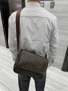 Vue détaillée du sac messager à carreaux marron porté sur l'épaule, montrant la sangle.
