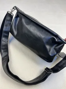 Black soft leather shoulder bag detail showing wide strap and metal hardware elements.