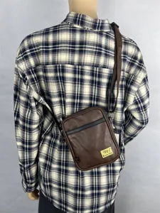 Detail view of brown vertical crossbody bag worn on back, featuring adjustable strap design.
