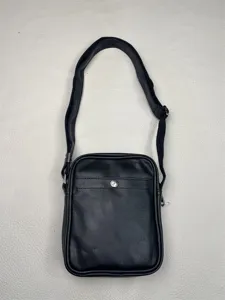 Detail view of black vertical crossbody bag featuring durable strap and metal snap button.