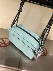 Light blue canvas crossbody shoulder bag, close-up view showing rope strap and zipper pocket details.