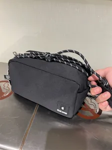 Black canvas crossbody bag detail shot, casual shoulder pouch with patterned rope strap.