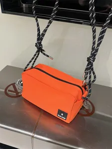 Close-up of orange canvas crossbody bag with black white rope strap and brand label detail.