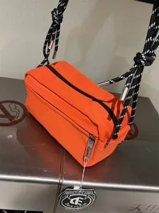 Detail shot of bright orange canvas crossbody shoulder bag with black white rope strap detail.