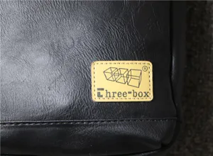 Close-up detail of black soft leather men bag with brand logo patch and texture view.