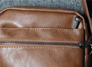 Detail view of brown men shoulder bag showing soft leather texture and metal zipper.