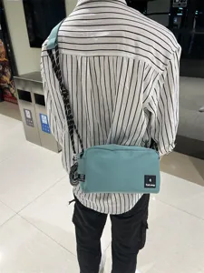 Detail view of a light blue canvas crossbody bag worn outdoors, showing its black and white strap.