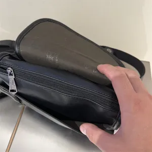 Vista dettagliata di una borsa a tracolla nera in pelle da uomo con tasca con zip e patta interna.