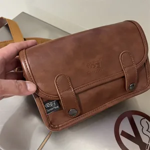 Dettaglio borsa a tracolla vintage marrone, borsetta da uomo compatta con fibbie doppie.