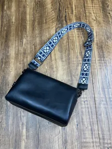 Vue détaillée d'un sac bandoulière souple pour homme avec sangle large à motif et accessoires.