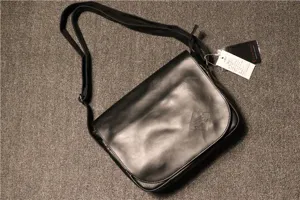 Details of the black leather men's messenger bag, showing the front flap and tag.