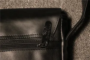Detail view of men's black PU leather messenger bag zipper pull and texture craftsmanship.