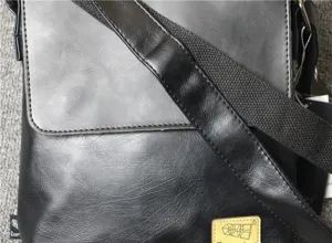 Detail view of black PU leather men messenger bag shoulder strap and brand logo patch texture closeup