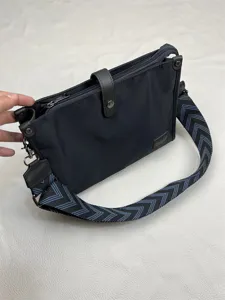 Black nylon crossbody bag with stylish wide patterned strap and leather snap closure detail.