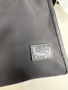 Black nylon crossbody shoulder bag detail view featuring brand logo patch and label.